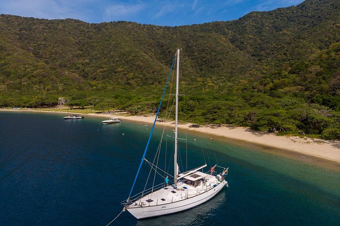 Large sailboat docked off a sandy, tree-lined shoreline.